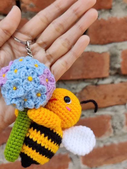 A custom-made keychain featuring a happy little bee holding a handmade hydrangea flower. The level of detail in the tiny petals was a fun challenge.