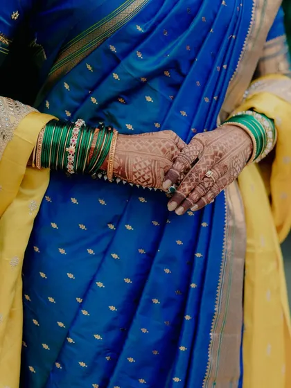 A detail shot focusing on the bride's hands, adorned with intricate henna and traditional green bangles, against her royal blue saree.