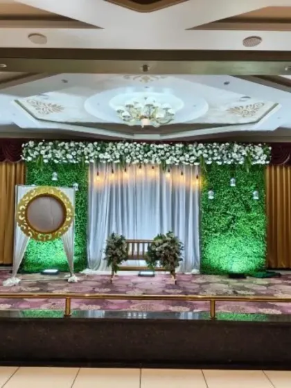 A simple yet elegant naming ceremony setup featuring a green foliage wall. The stage is kept clean with a white floral garland at the top and a beautifully decorated cradle in the center.