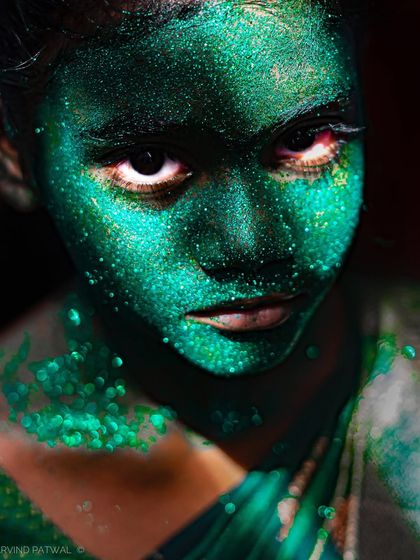 A young girl's face covered in green glitter for a festival performance. Her intense, direct gaze creates a haunting and beautiful portrait that stays with you.
