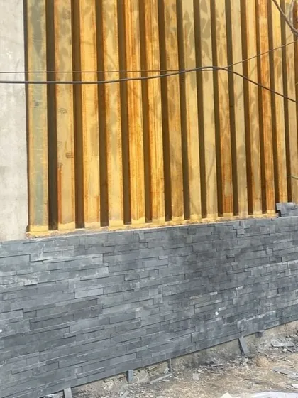 A corner detail of the finished wall, combining dark stone cladding with vertical wooden slats for a modern, textured look.