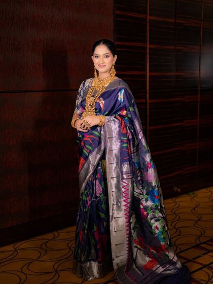 The complete look, showcasing the beautiful drape of the floral Paithani saree. The makeup is kept timeless and elegant to complement the vibrant colors of the outfit.
