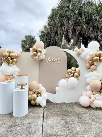 A chic and minimalist outdoor baby shower setup. This design uses neutral backdrops, a crescent moon prop, and a simple balloon arrangement in white, beige, and gold for an understated, elegant look.