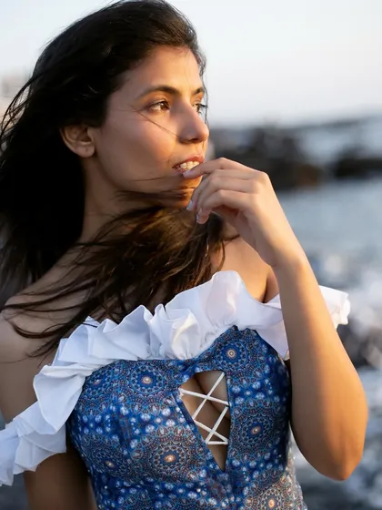 A close-up portrait that feels candid and thoughtful. The wind in the hair and the soft, natural light create an intimate mood, perfect for showcasing the details of the ruffled, off-the-shoulder top.