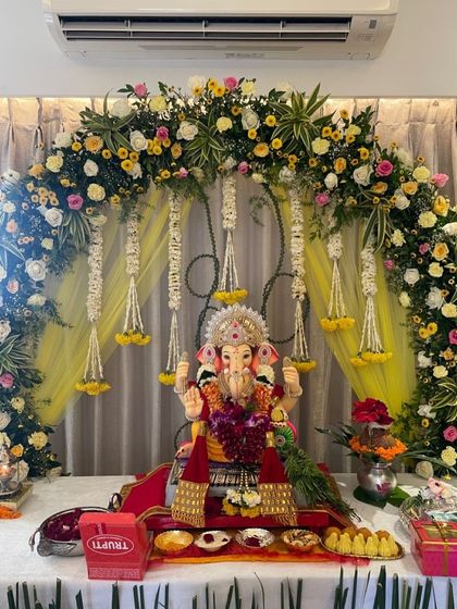 A traditional Ganpati decor setup with a vibrant arch of yellow and pink flowers, complemented by hanging jasmine strings.