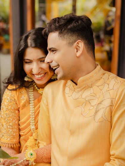 A joyful moment from a Haldi ceremony. The groom's custom yellow kurta features subtle, elegant embroidery on the collar, perfectly in sync with the bride's vibrant attire.