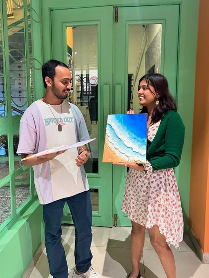 A proud moment for a creator, holding up her finished ocean wave painting. Our workshops are designed for you to leave with a piece of art you're truly happy with.