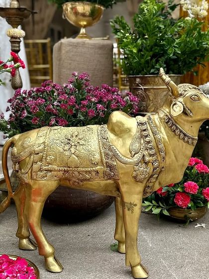 A beautifully detailed brass Nandi statue, a symbol of divinity and strength, surrounded by vibrant pink and white flowers.