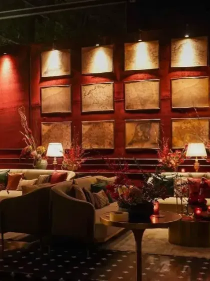 We designed multiple lounge areas to encourage conversation. This setup features plush sofas, a dramatic art wall lit from above, and deep red velvet curtains, creating a cozy and sophisticated corner within the larger event space.