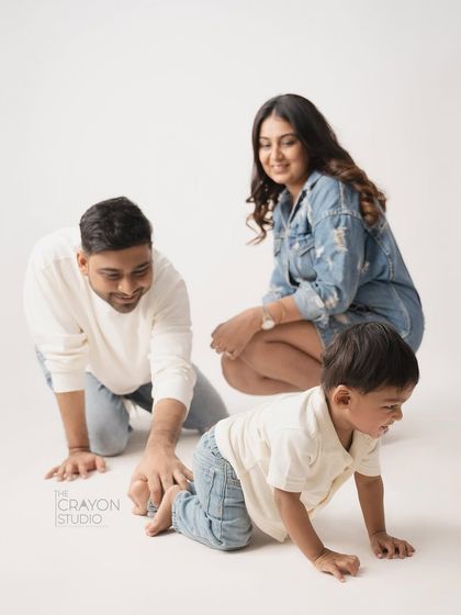 Getting down on the floor to play is a wonderful way to connect. This candid shot captures a family crawling and laughing together, showing their fun-loving spirit in a clean studio setting.