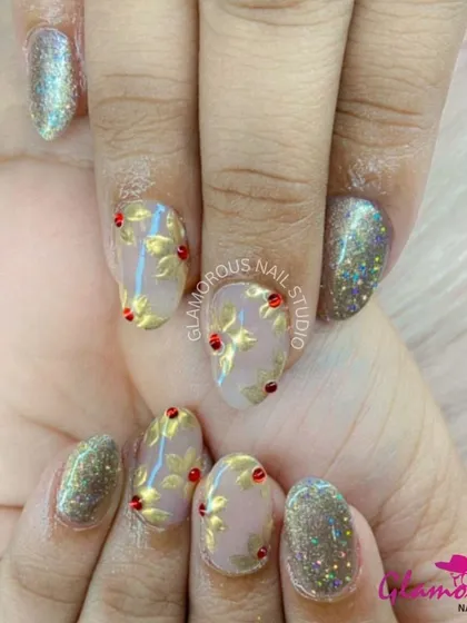 Golden leaves and a touch of sparkle. This elegant design features a sheer nude base with gold-leaf floral patterns, accented with red gems and full-coverage glitter nails.