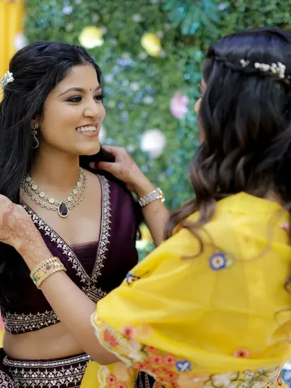 A sweet moment between sisters. The bride's makeup is soft and radiant, designed to complement her deep purple lehenga without overpowering her features.