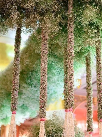 A ceiling of baby's breath creates a cloud-like effect. This installation features thick columns of flowers hanging from the ceiling, adding a magical and ethereal quality to the event space.