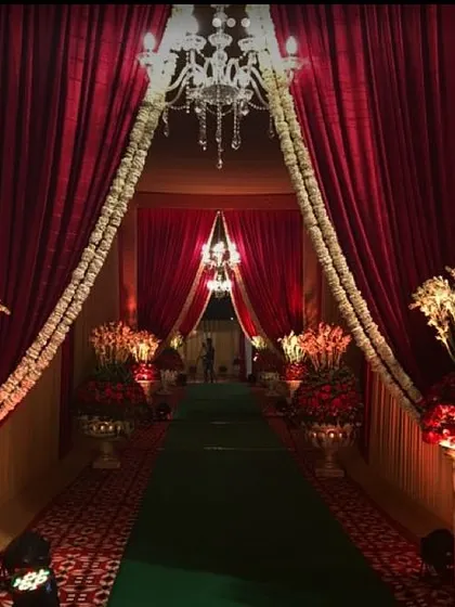 This royal entrance features deep red curtains, large floral arrangements in traditional vases, and a green carpet. The design is perfect for creating a sense of grandeur and heritage.