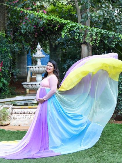 A magical "flying fabric" shot with our rainbow gown in a garden setting, with a fountain in the background.