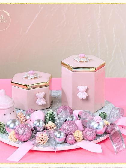 A full view of the sparkling baby girl announcement hamper. The arrangement includes a baby bottle-shaped ceramic, hexagonal jars, and a platter full of festive baubles, creating a truly celebratory feel.