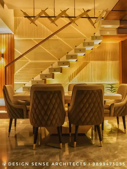 A symmetrical shot of a dining setup, emphasizing the elegant quilted chairs and the dramatic, beautifully lit staircase in the background that acts as a sculptural element.