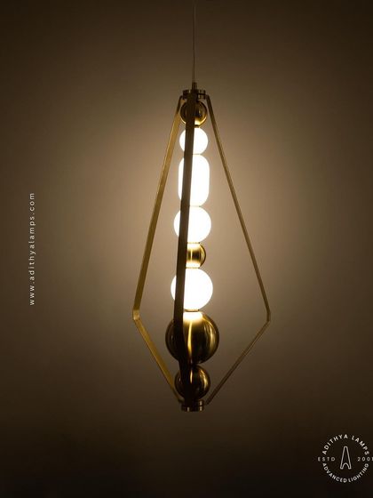 This elegant pendant is framed by a triangular gold structure, enclosing a string of white and gold beads. It's a sophisticated and modern piece that adds a touch of jewelry-like decoration to your space.