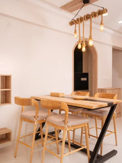 The dining area at Mana Capitol showcases a rustic-modern aesthetic with a live-edge style table, high chairs, and a unique rope and bulb chandelier.