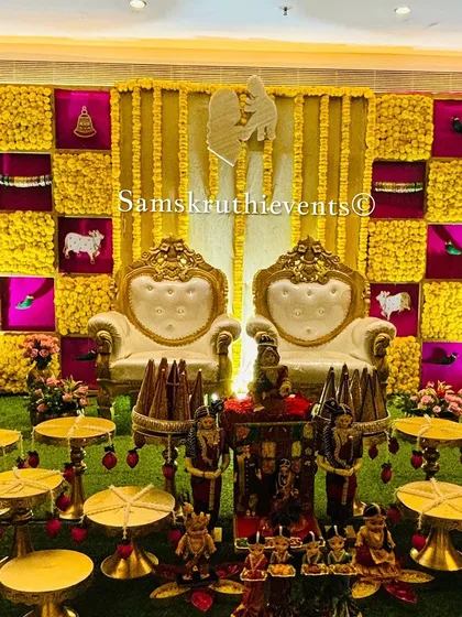 A unique baby shower setup with a yellow and pink checkerboard backdrop. The stage features two thrones and a creative display of offerings on small tables, perfect for a modern ceremony.