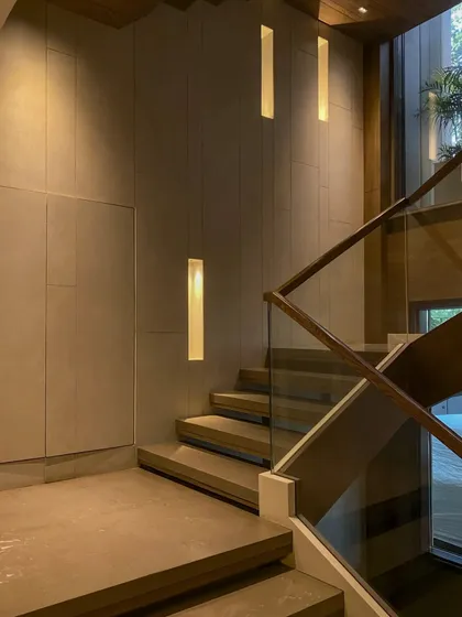 A closer look at the staircase, highlighting the integrated wall lighting and the clean lines of the glass and wood railing. Every element is designed to be both functional and beautiful.