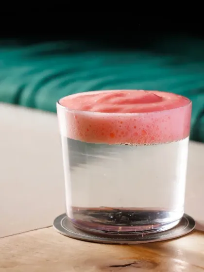 This unique drink features a clear base with a distinct, flavorful pink foam layered on top, creating a beautiful contrast of color and texture.