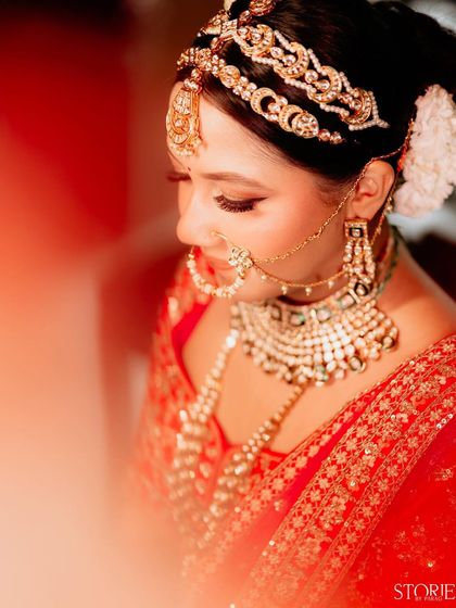 A close-up, dreamy portrait of a bride looking down. The warm, red-toned light leak effect adds an artistic and romantic feel, highlighting her stunning jewelry and delicate features.