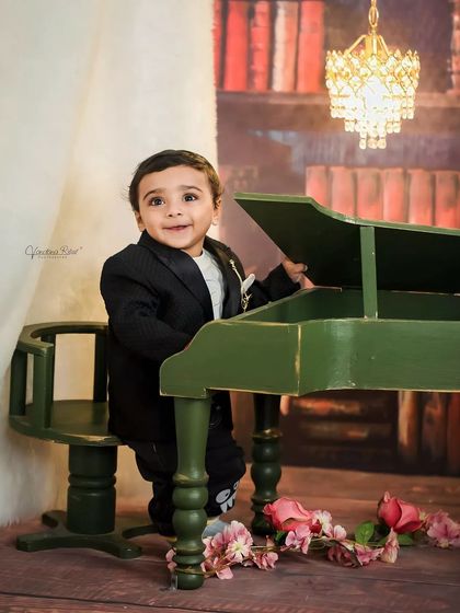 This little gentleman looks dapper in his suit, posing with a miniature piano. The classic library-themed backdrop with a chandelier adds a touch of elegance to this creative toddler portrait.
