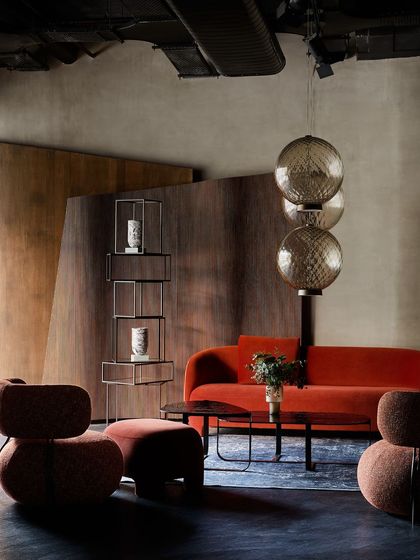 This vignette showcases a bold, orange-red sofa and sculptural armchairs. The design plays with color and form, using statement lighting and a metal-and-wood bookshelf to complete the modern, artistic look.