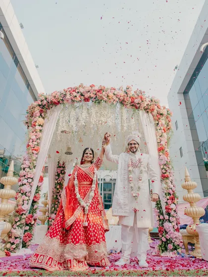 A triumphant exit from a grand Gujarati wedding ceremony. This shot captures the scale of the celebration, from the floral mandap to the shower of petals, marking the beginning of a new journey.
