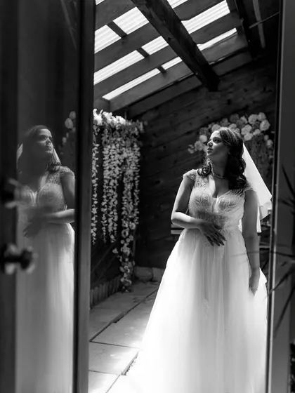 A thoughtful black and white portrait of the bride in her white wedding gown. The reflection in the door adds a layer of depth and artistry to the image.
