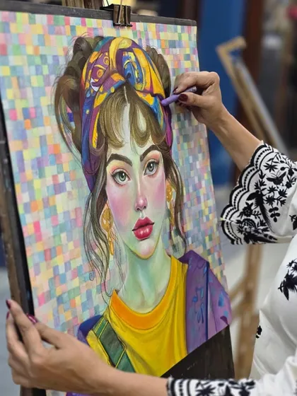 This image captures the artist's focused expression as she applies the final touches to the hair and turban in her vibrant oil pastel portrait.
