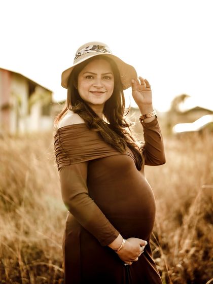 A beautiful golden-hour portrait of the mom-to-be in a stylish hat, smiling warmly at the camera. She is absolutely glowing.