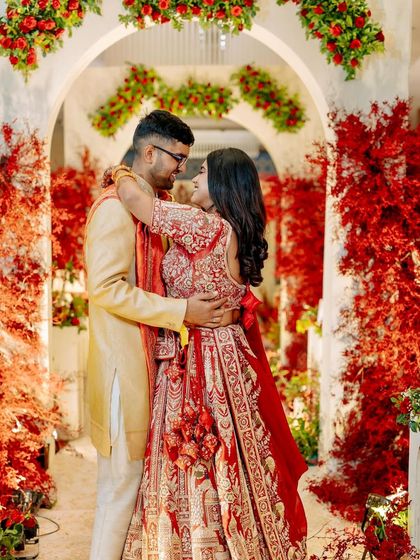 A romantic portrait of the couple at their reception, framed by white arches and dramatic red foliage that creates a stunning visual contrast.