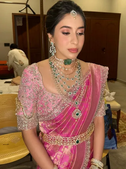 A dreamy pink-hued bridal look for a Muhurtham that is both classic and contemporary. The soft pink eyeshadow and lip color beautifully complement her emerald jewelry.