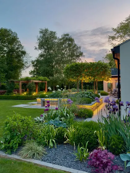 A duplicate view of a beautifully lit garden at dusk. The combination of architectural plants and carefully placed lighting creates a stunning visual effect, ensuring the garden is a focal point day and night.
