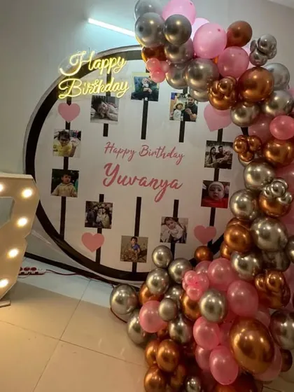 A personalized 3rd birthday with a photo display backdrop and a balloon arch in pink and metallic colors.
