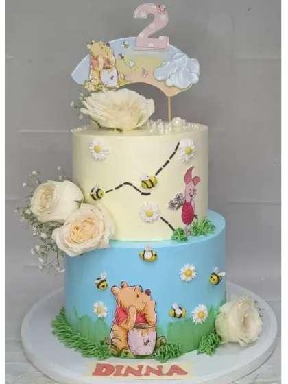 A tall, two-tier Winnie the Pooh cake perfect for a second birthday. This choco-vanilla cake features Pooh and his friends in the Hundred Acre Wood, decorated with fresh flowers for a soft, storybook feel.