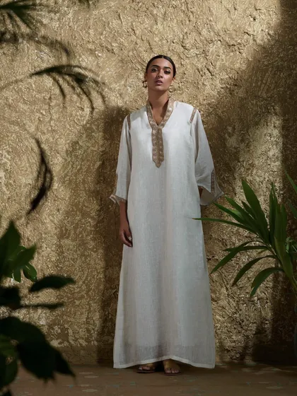A flowing white kaftan with delicate gold embroidery at the neckline. This look embodies effortless elegance and is a staple of modern resort wear.