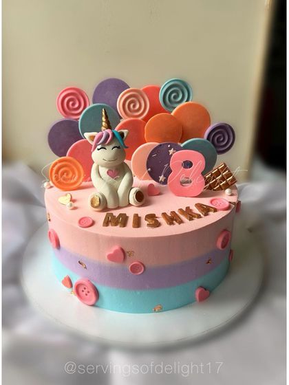 A unique unicorn cake surrounded by a white chocolate candy paradise. The pastel rainbow stripes and cute fondant unicorn make it a magical centerpiece.
