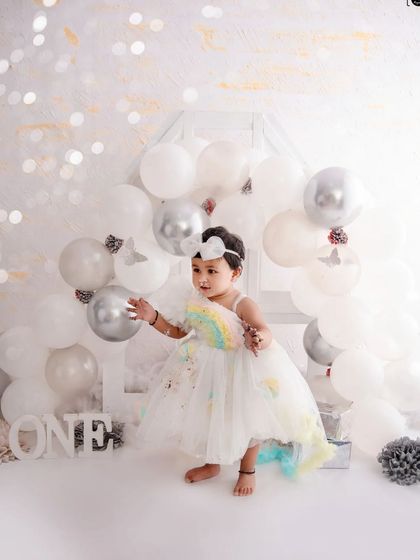 A whimsical first birthday shoot with a dreamy all-white theme, featuring silver balloons and delicate butterfly details.