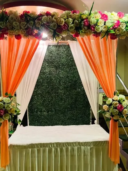 This unique mandap combines a classic canopy structure with a modern textured backdrop. The background panel is made of artificial green grass, which contrasts beautifully with the peach and white floral arrangement.