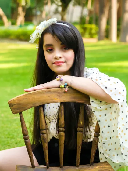 A young girl poses confidently with a wooden chair in a green, sunny park. A beautiful and classic outdoor portrait.