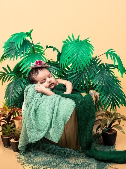 A creative newborn portrait with a jungle or tropical theme. The baby is peacefully asleep, wrapped in green, surrounded by lush plants.