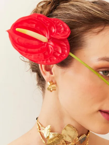 The vibrant red of the anthurium flower creates a striking contrast against the model's skin and the gold jewelry.