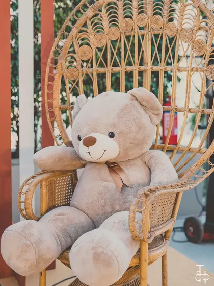 A giant, cuddly teddy bear seated in a peacock chair, serving as a cute and welcoming prop for the baby shower.