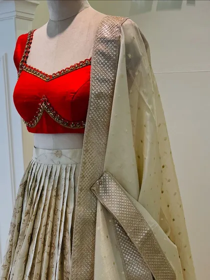 Elegance in every fold. This ivory tissue lehenga with a subtle gold print is paired with a vibrant red katori blouse. The contrast creates a look that is both traditional and incredibly chic.