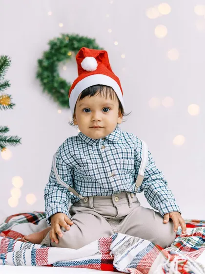 Another angle of the little boy in his Santa hat, sitting on a festive plaid blanket.