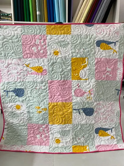A whimsical baby quilt with whale and sun prints, finished with an all-over swirl quilting pattern.