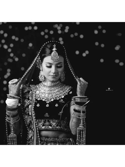 An elegant black and white portrait of the bride adjusting her dupatta. The soft bokeh in the background and the focus on her intricate jewelry create a classic and graceful image.